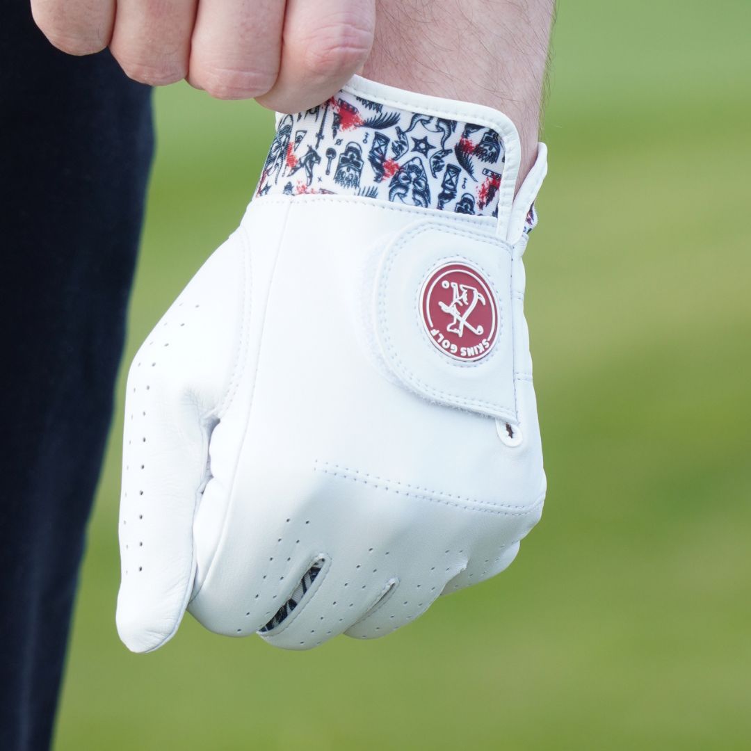 White golf glove with a red logo held by a person on a blurred green background