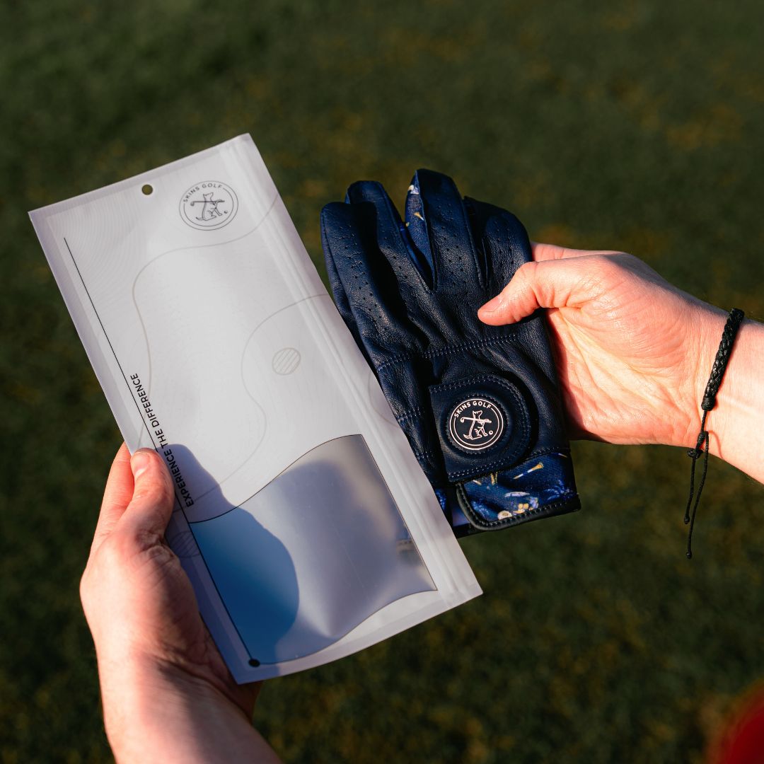 Person holding a navy glove and its packaging with a brand logo against a grassy background
