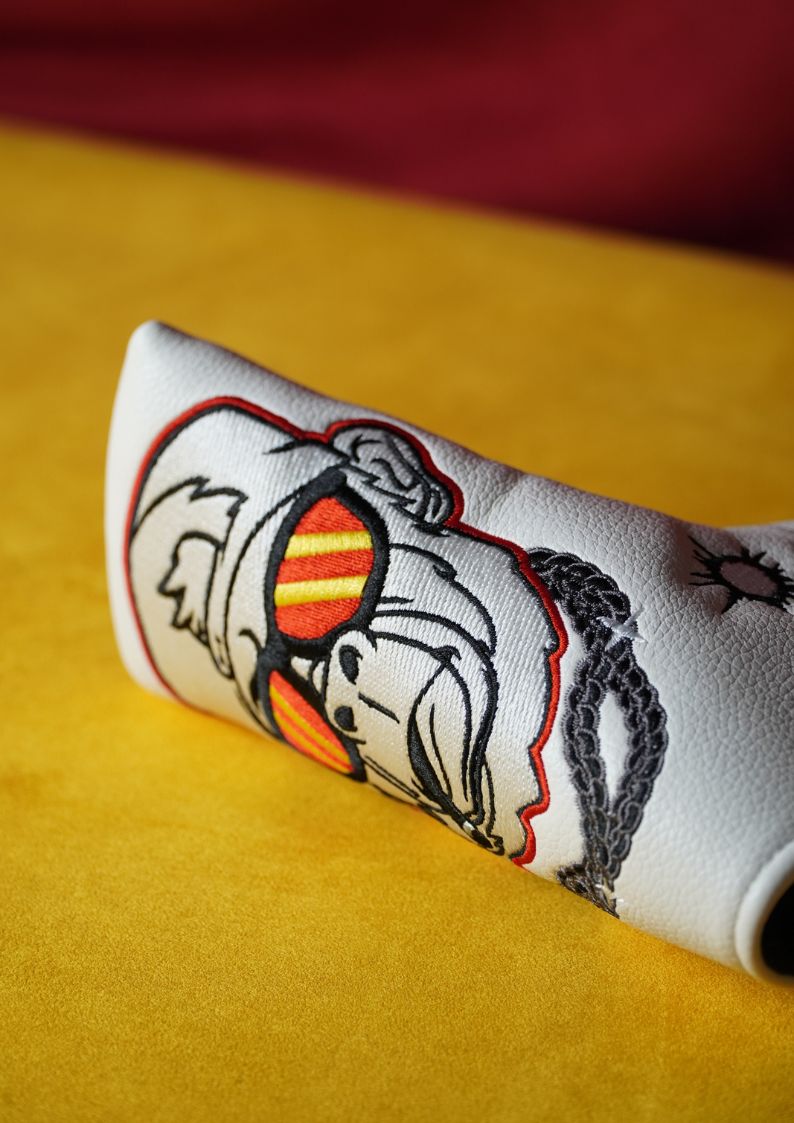 White golf headcover with embroidered design on a yellow surface