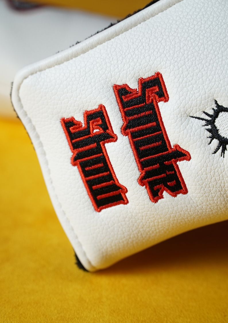 White golf headcover with red and black embroidered designs on a yellow background