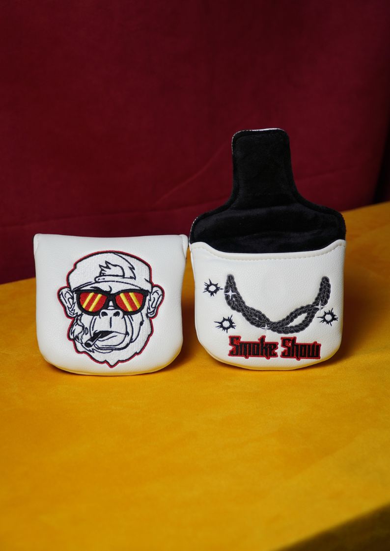 Two white golf putter headcovers featuring monkey graphics and text on a yellow surface.