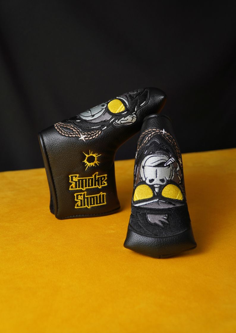 Two black golf club head covers with graphic designs on a yellow surface.