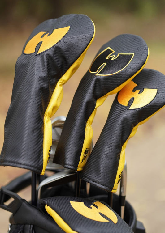 A close-up of golf club headcovers with black and yellow Wu-Tang Clan themed headcovers on the clubs, set against a blurred outdoor background.