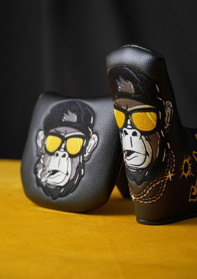 Two black putter headcovers with monkey designs wearing sunglasses on a yellow surface.