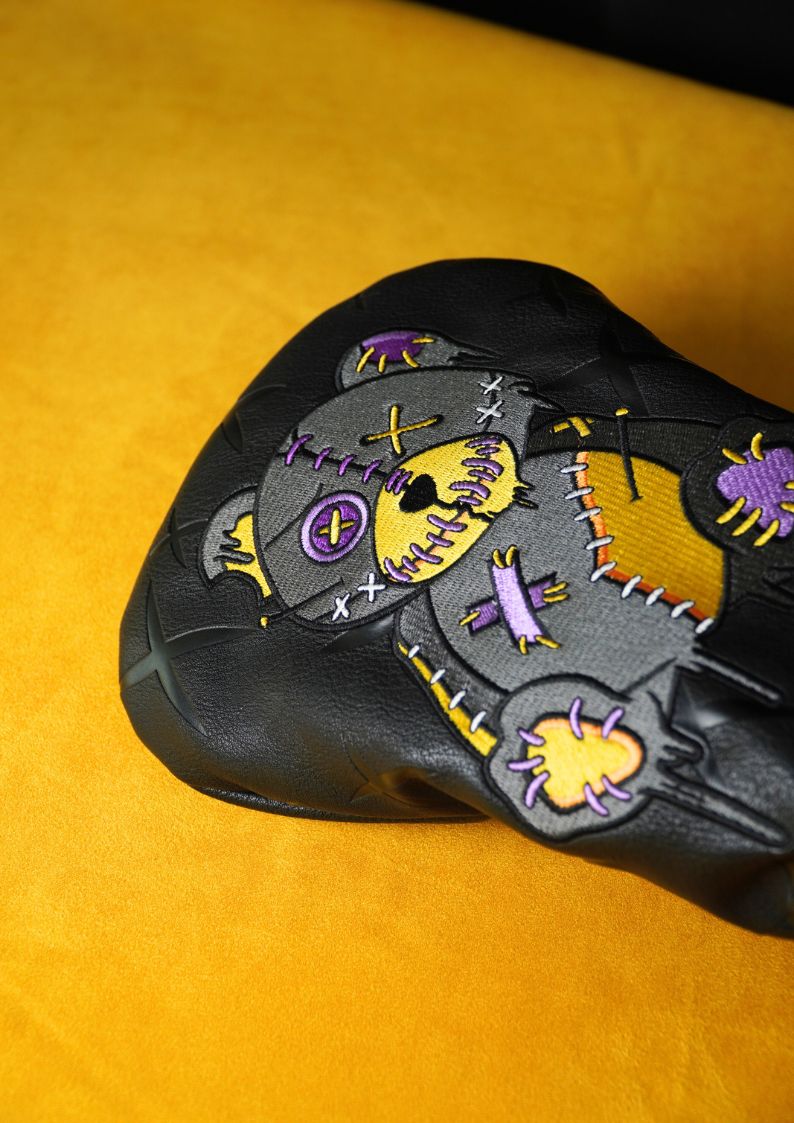 Black driver headcover with colorful patch design on a yellow background