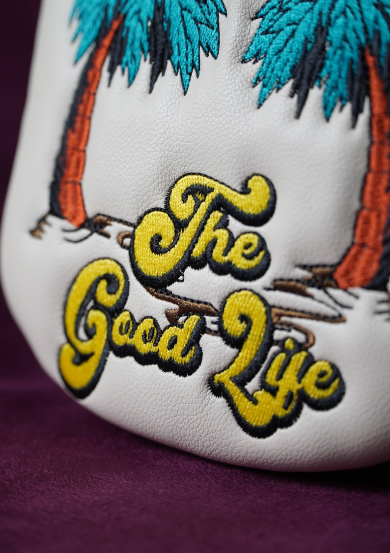 Embroidered detail on a golf headcover with 'The Good Life' text and palm trees on a purple background.