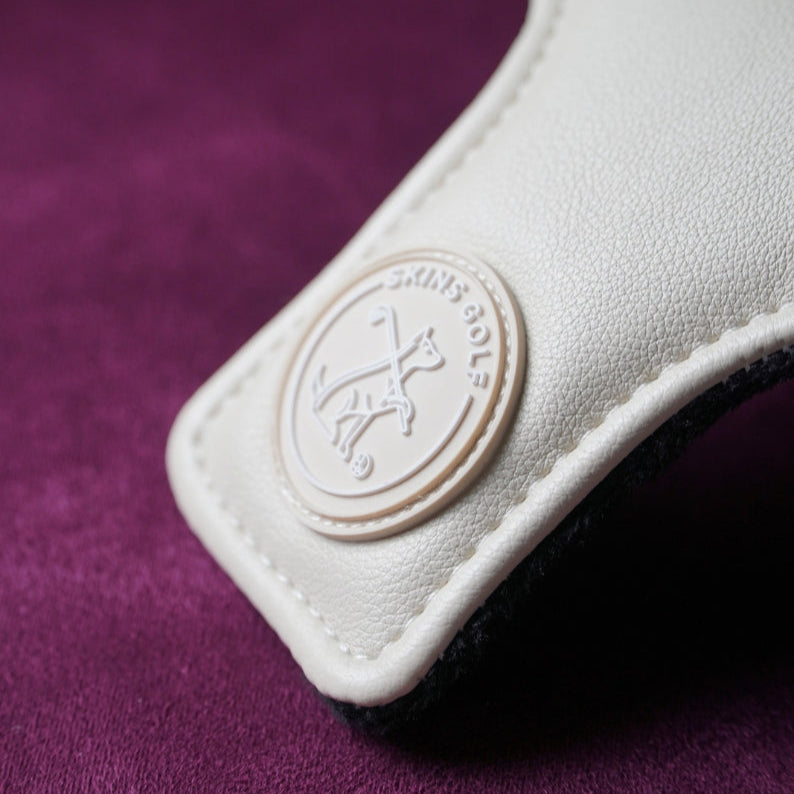 Close-up of a white golf headcover with a brand logo on a purple background