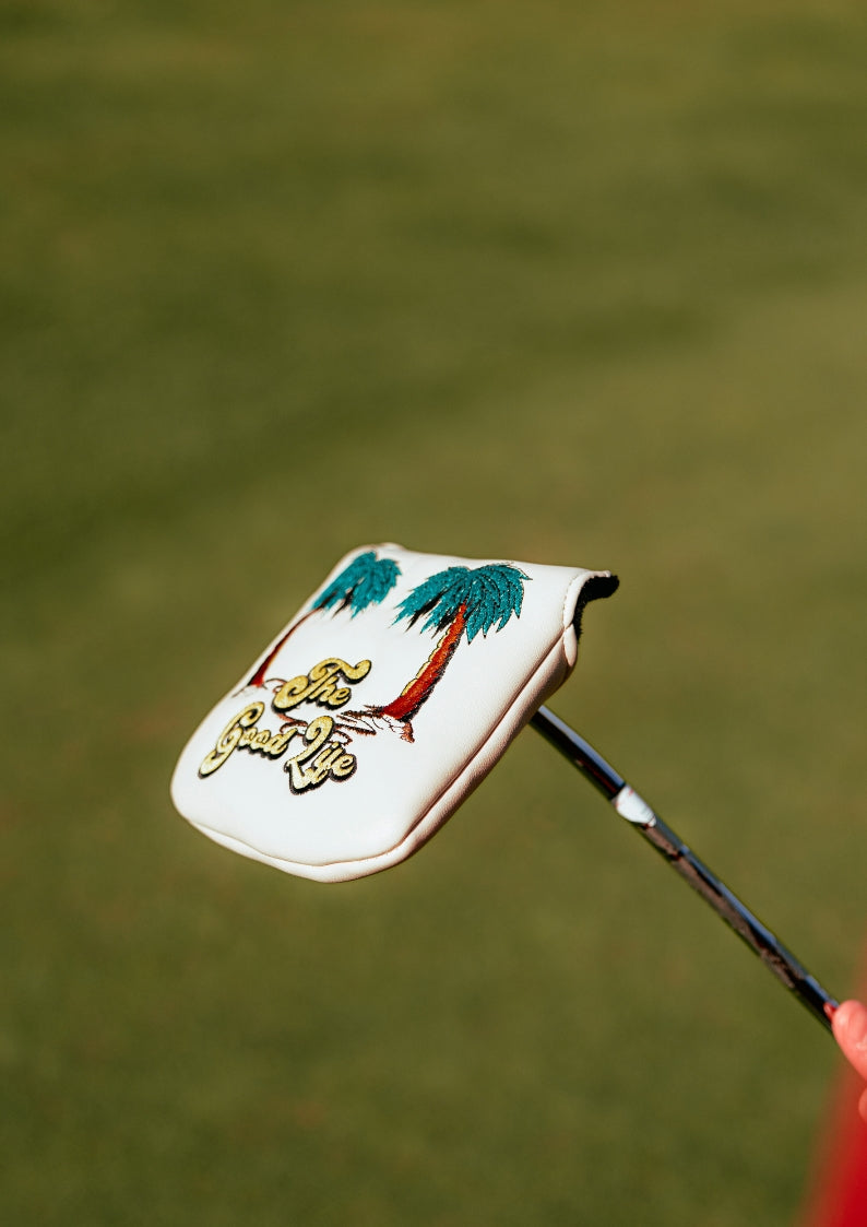 Golf club head cover with palm tree design on a blurred green background