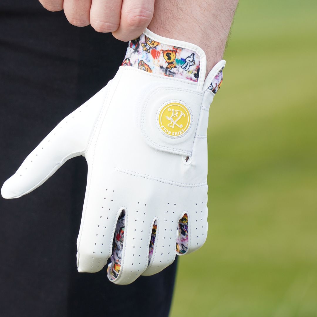 White glove with colorful patterned cuff held by a person against a blurred green background