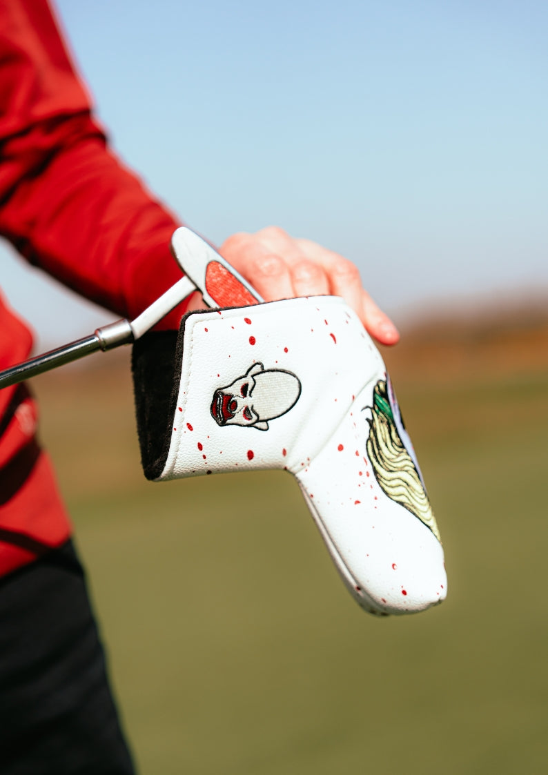 Golf club head cover with Joker design held by a person on a blurred golf course background