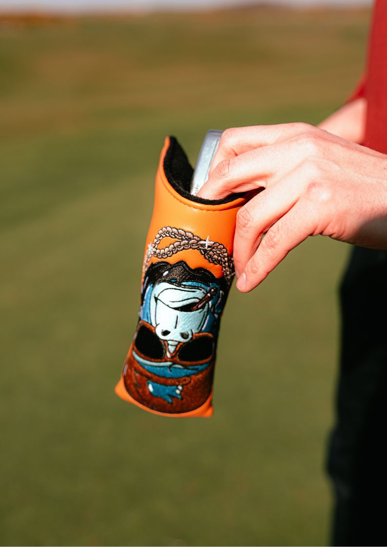 Hand holding a colorful golf headcover with a unique design on a grassy background