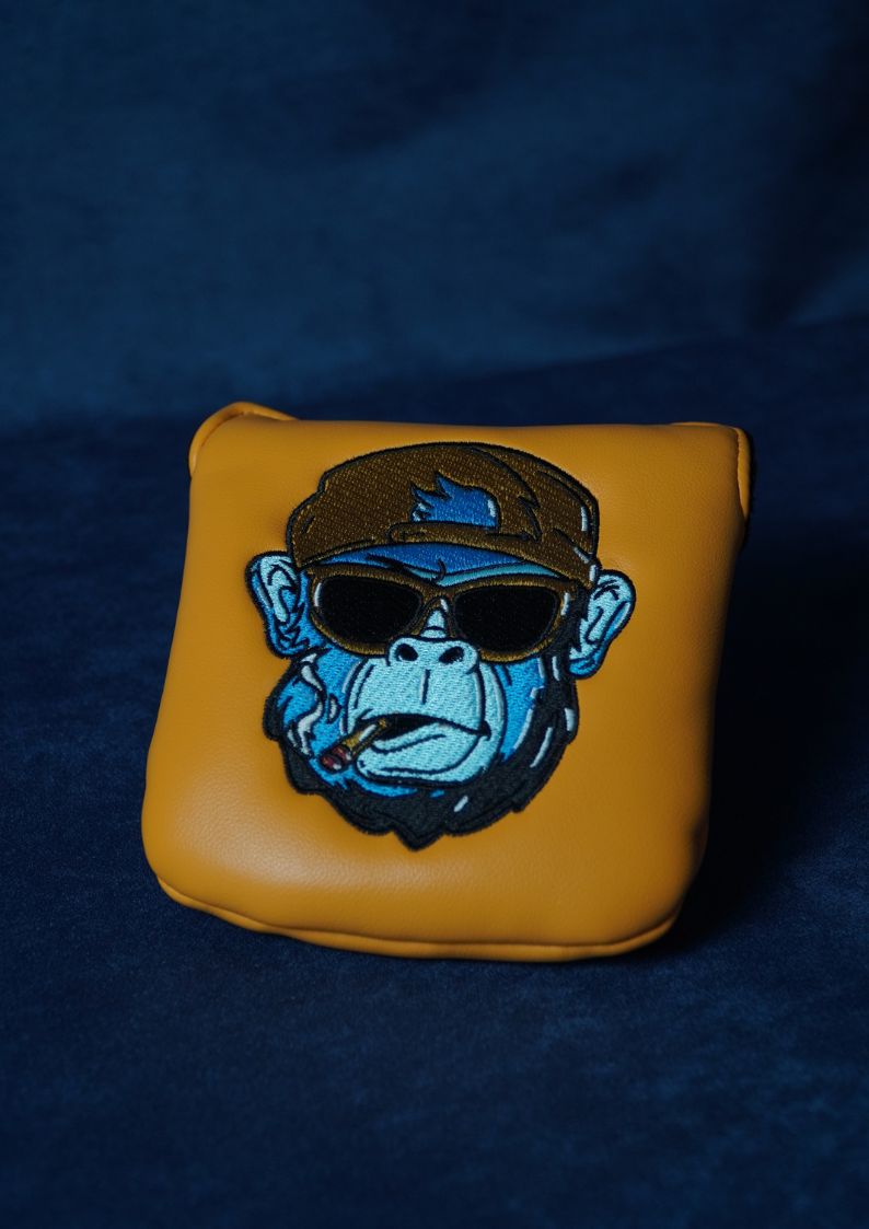 Yellow golf headcover with a monkey wearing sunglasses and a cap on a dark blue background
