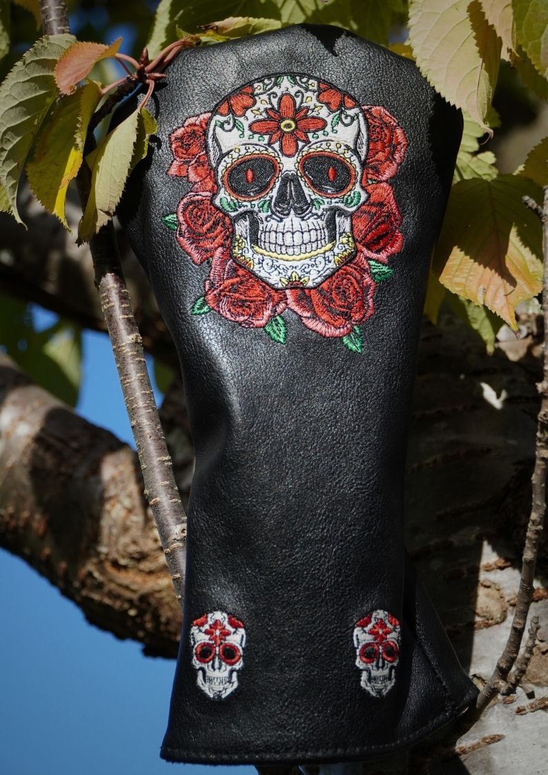 Black leather golf club head cover with skull and rose design on a natural background