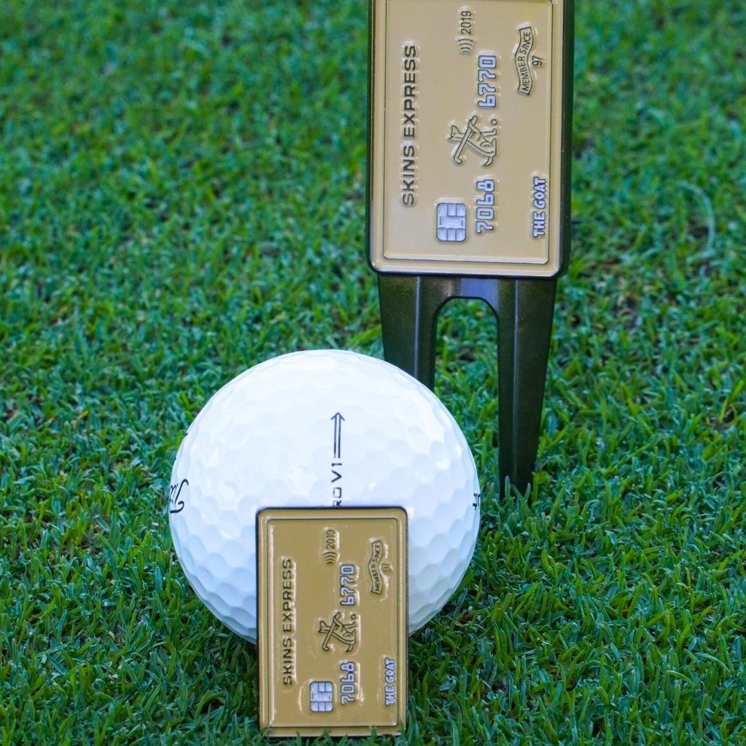 Golf ball marker and divot tool on grass with gold credit card design