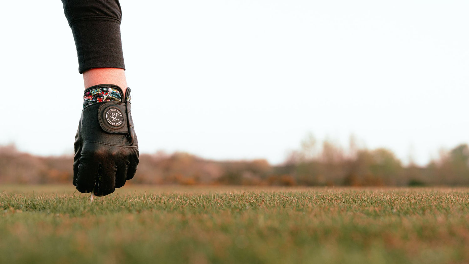 black golf glove teeing up a ball