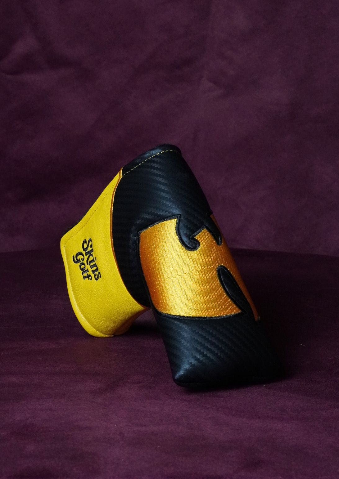 A single golf headcover by Skins Golf, featuring a black carbon-fiber pattern and a metallic gold Wu-Tang Clan logo, displayed on a dark purple textured background.