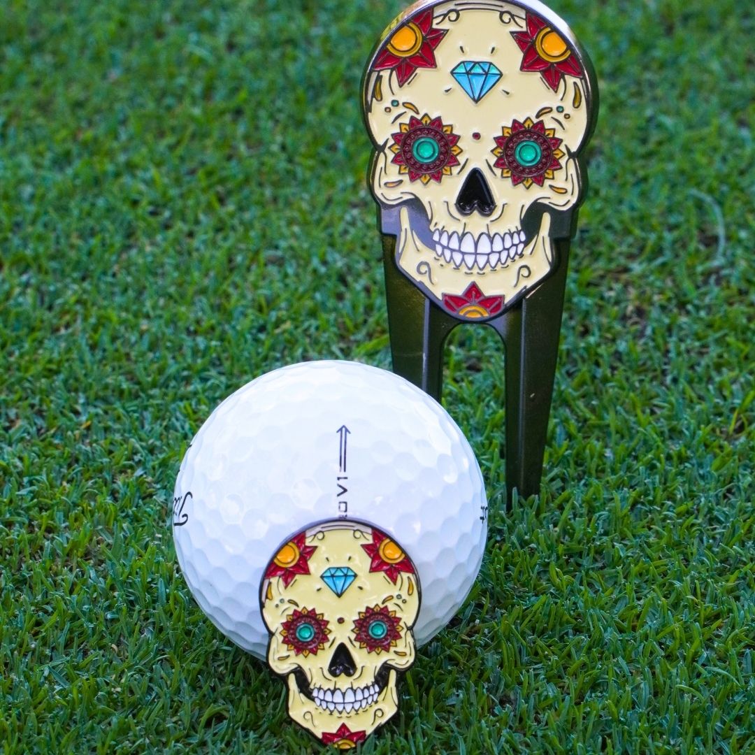 Golf ball marker with colorful skull design on grass