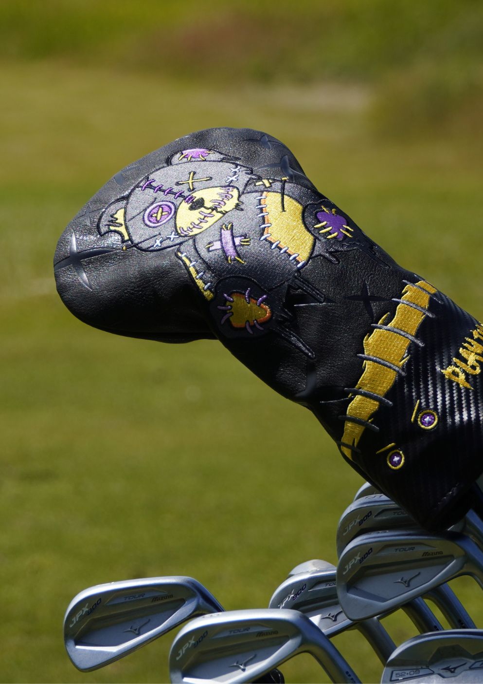 Golf club head cover with decorative patterns on a grass background