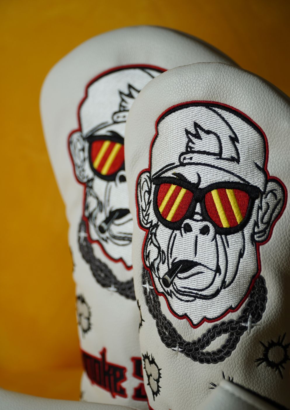 Two white golf headcovers with monkey designs wearing sunglasses on a yellow background