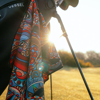 Colorful patterned towel draped over a golf bag on a golf course.
