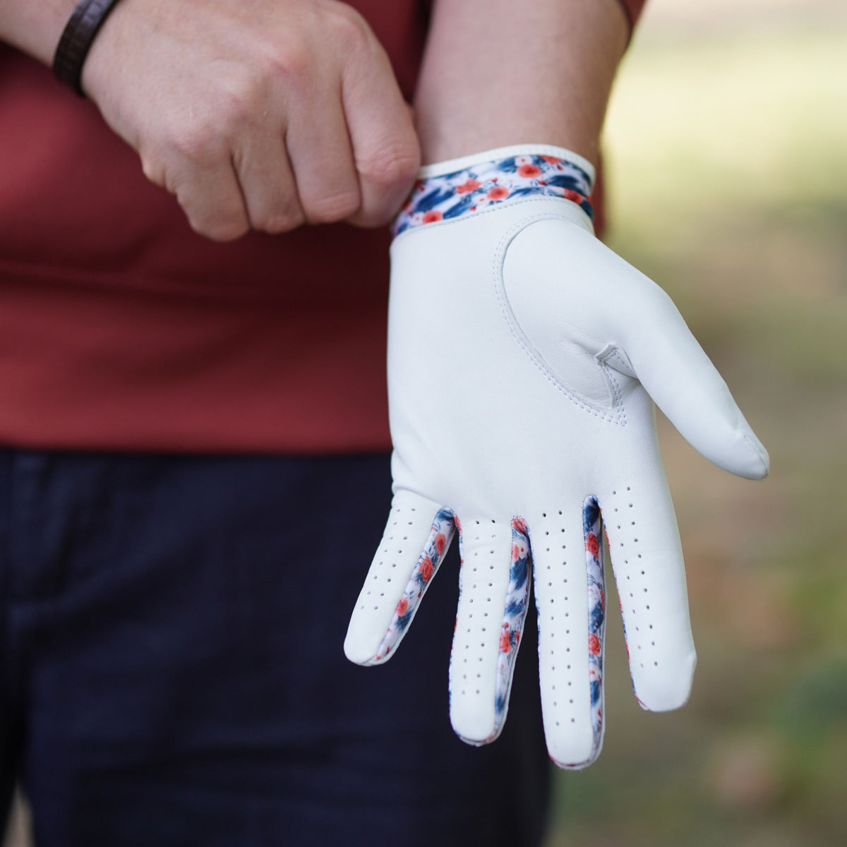 A white golf glove with red and blue floral patterned trim on the cuff and between the fingers, being worn on a person's hand.