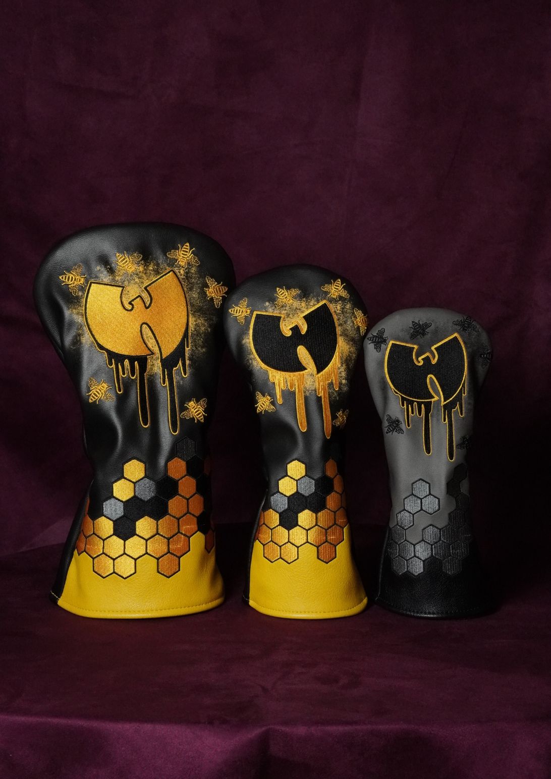 Three black and gold Wu-Tang Clan themed golf club headcovers arranged by size on a dark purple velvet background.