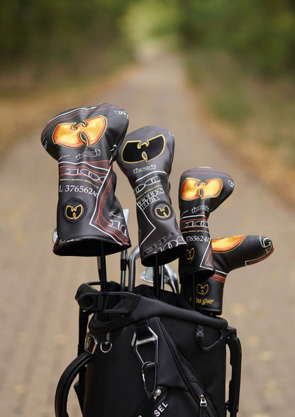 A black golf bag on a blurred outdoor path with three golf club headcovers standing out, featuring a gold and black Wu-Tang Clan logo design.
