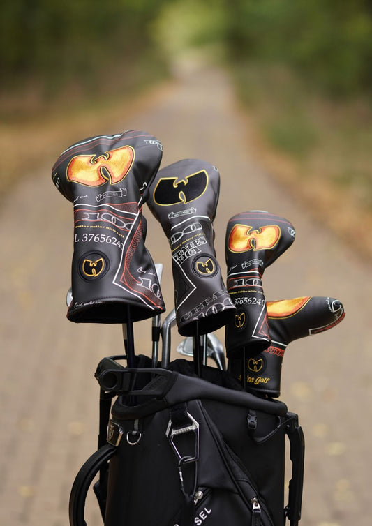A black golf bag on a blurred outdoor path with three golf club headcovers standing out, featuring a gold and black Wu-Tang Clan logo design.