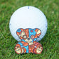 Golf ball with a colorful voodoo bear design ball marker on grass