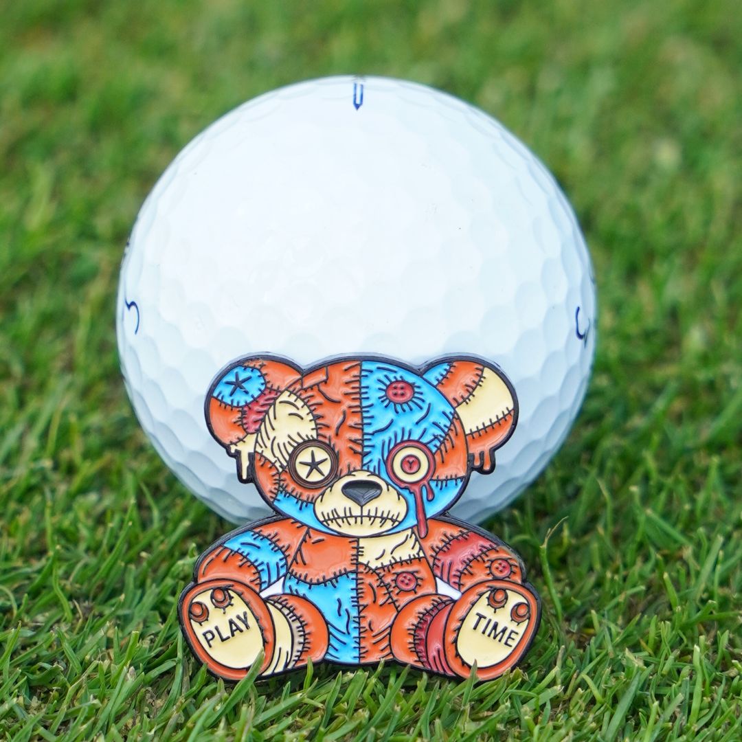 Golf ball with a colorful voodoo bear design ball marker on grass