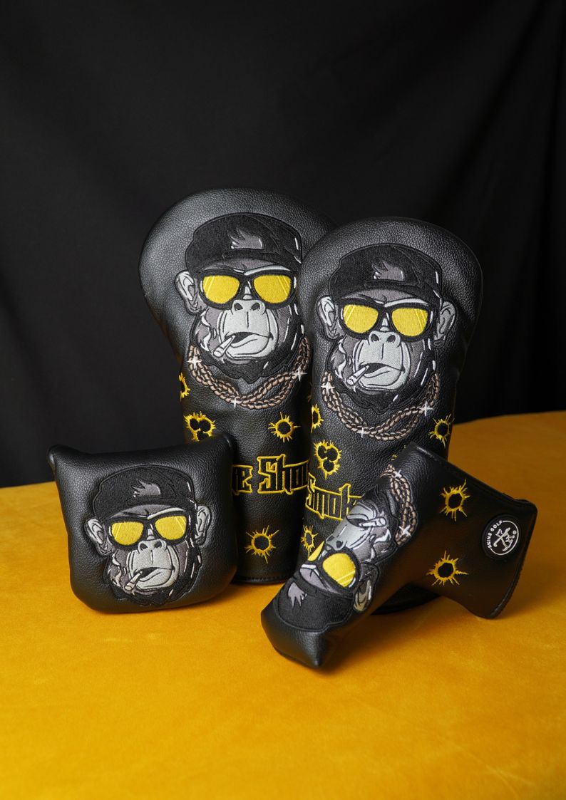 Four golf club headcovers with monkey designs and yellow sunglasses on a black and orange background