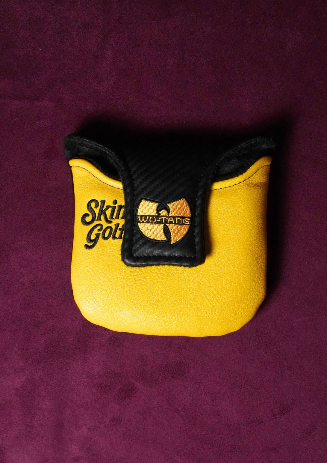 A yellow and black Wu-Tang Clan themed golf mallet headcover on a textured dark purple background.