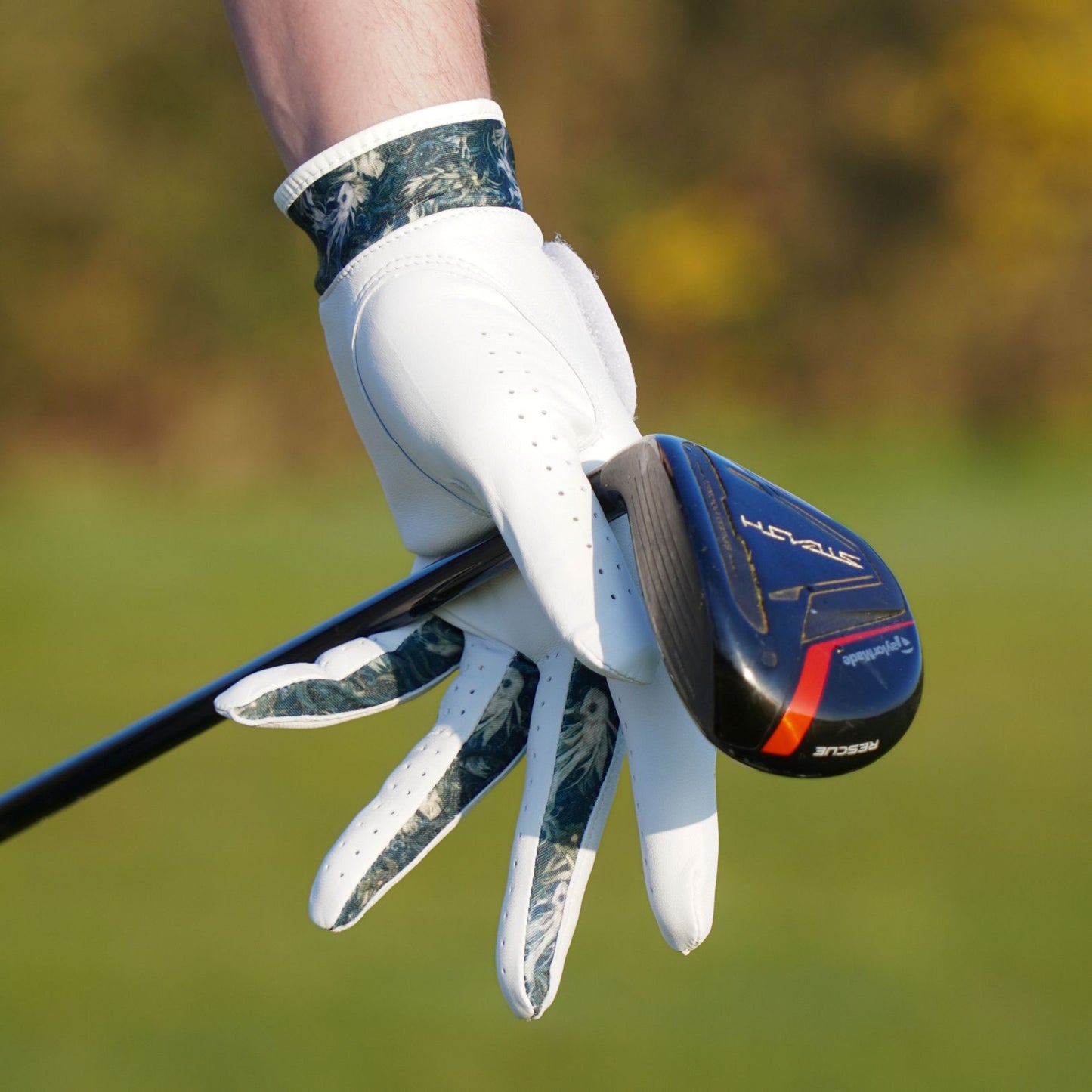 Golf club with a gloved hand on a blurred golf course background