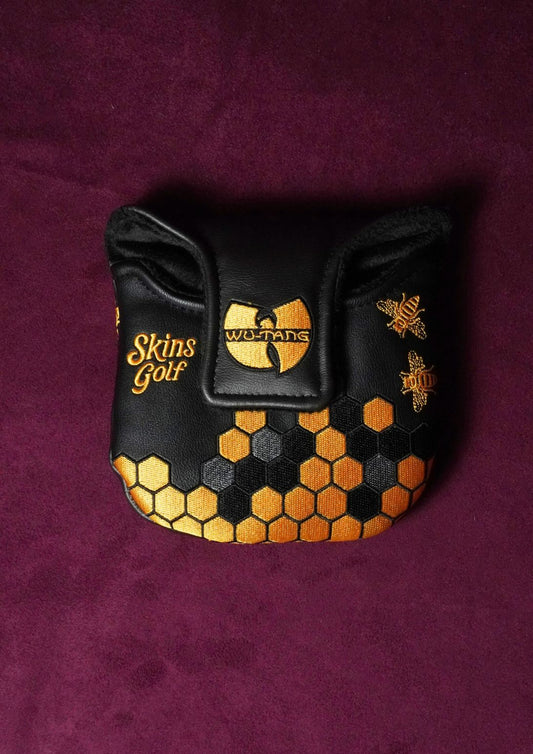 A black leather golf club headcover featuring gold embroidery with the Wu-Tang Clan logo, 'Skins Golf' text, and a honeycomb pattern at the bottom, displayed on a textured dark purple background.
