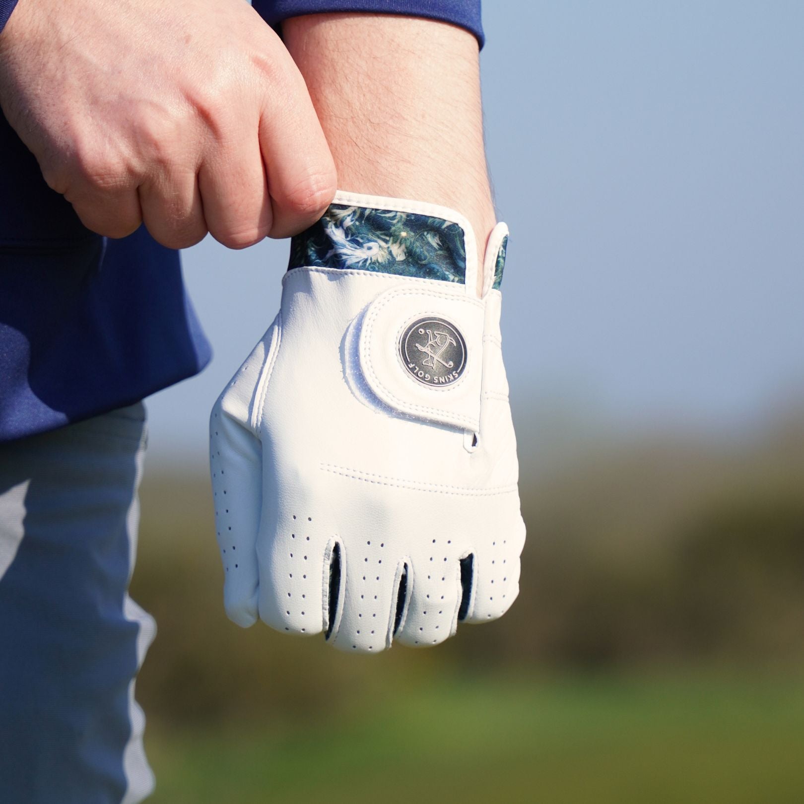 White golf glove held by a person on a blurred outdoor background