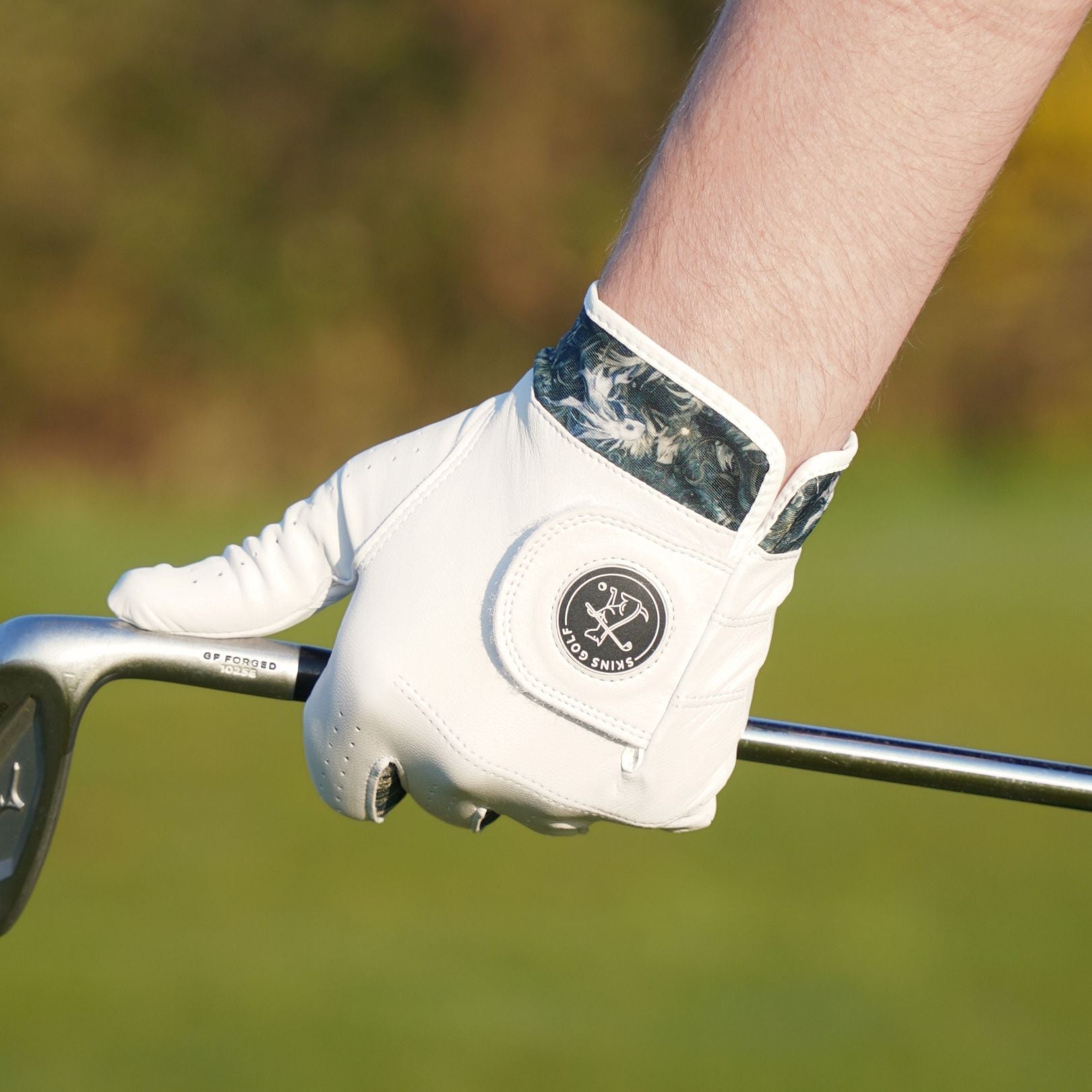 Close-up of a person's hand wearing a white golf glove holding a golf club on a blurred green background