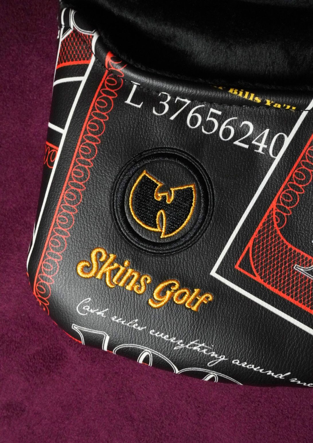 Close-up of a mallet headcover featuring a gold Wu-Tang Clan logo, 'Skins Golf' text, resting on a textured purple surface.