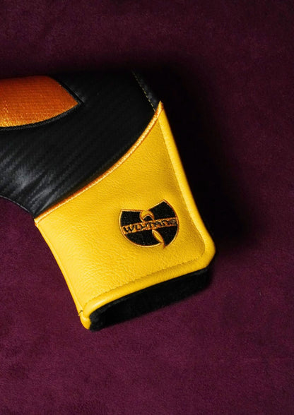 A close-up of a golf headcover featuring a yellow and black color-blocked design with a black and gold Wu-Tang Clan logo on the cuff, set against a dark purple textured background.