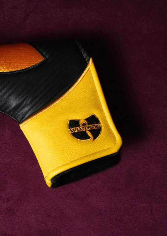 A close-up of a golf headcover featuring a yellow and black color-blocked design with a black and gold Wu-Tang Clan logo on the cuff, set against a dark purple textured background.