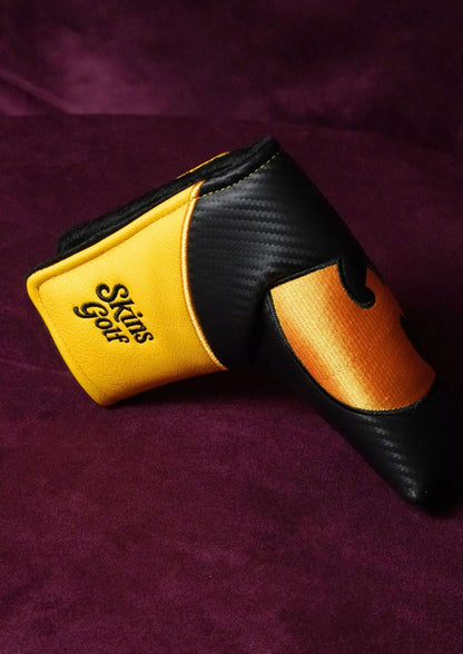 A Skins Golf headcover in black and yellow, featuring a carbon fiber pattern on the black sections and a textured yellow panel on the back, resting on a dark purple velvet background.