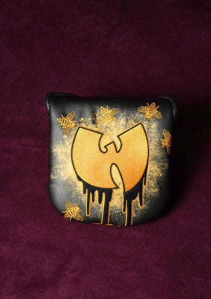 A black leather mallet headcover featuring a gold dripping Wu-Tang Clan logo, surrounded by gold spray-painted bees, displayed on a textured dark purple velvet background.