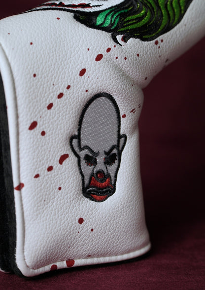 Close-up of a white golf headcover with a Joker design and red specks on a dark background