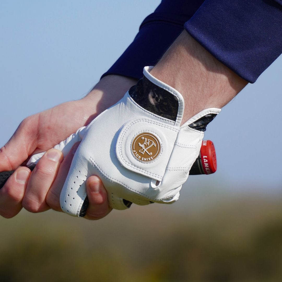 Hand wearing a white golf glove with a red label, holding a golf club on a blurred outdoor background.