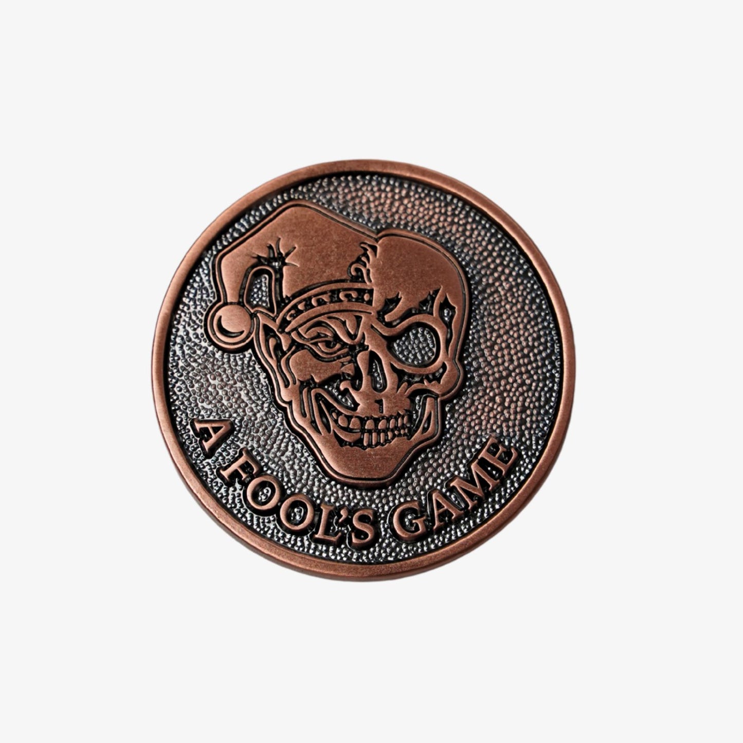Copper golf ball marker with skull design and 'A Fool's Game' text on a white background
