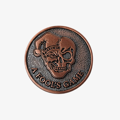 Copper golf ball marker with skull design and 'A Fool's Game' text on a white background