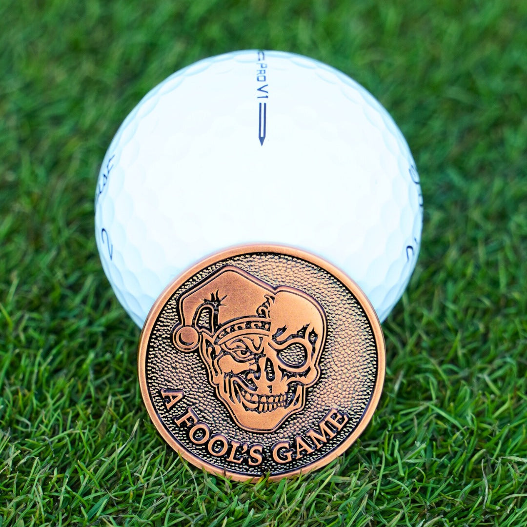 Copper golf ball marker with skull design on a white golf ball on grass