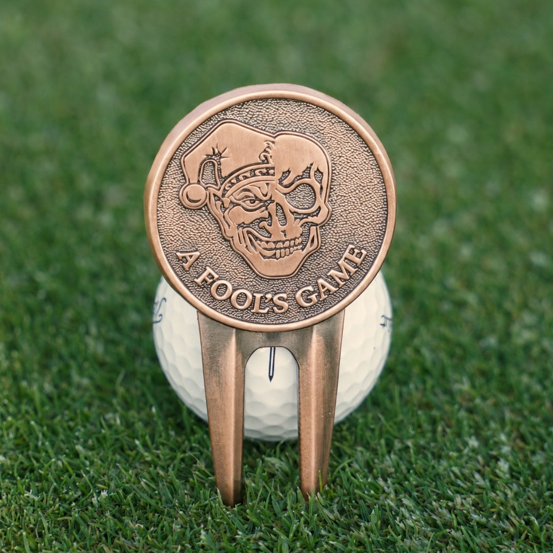 Bronze golf divot tool with skull design on a golf ball on grass