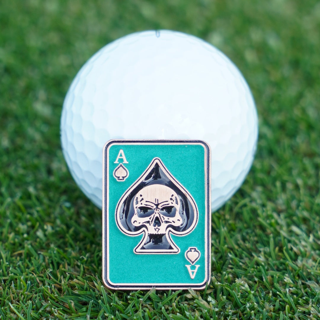 Golf ball with a ball marker featuring a skull and spades design on grass