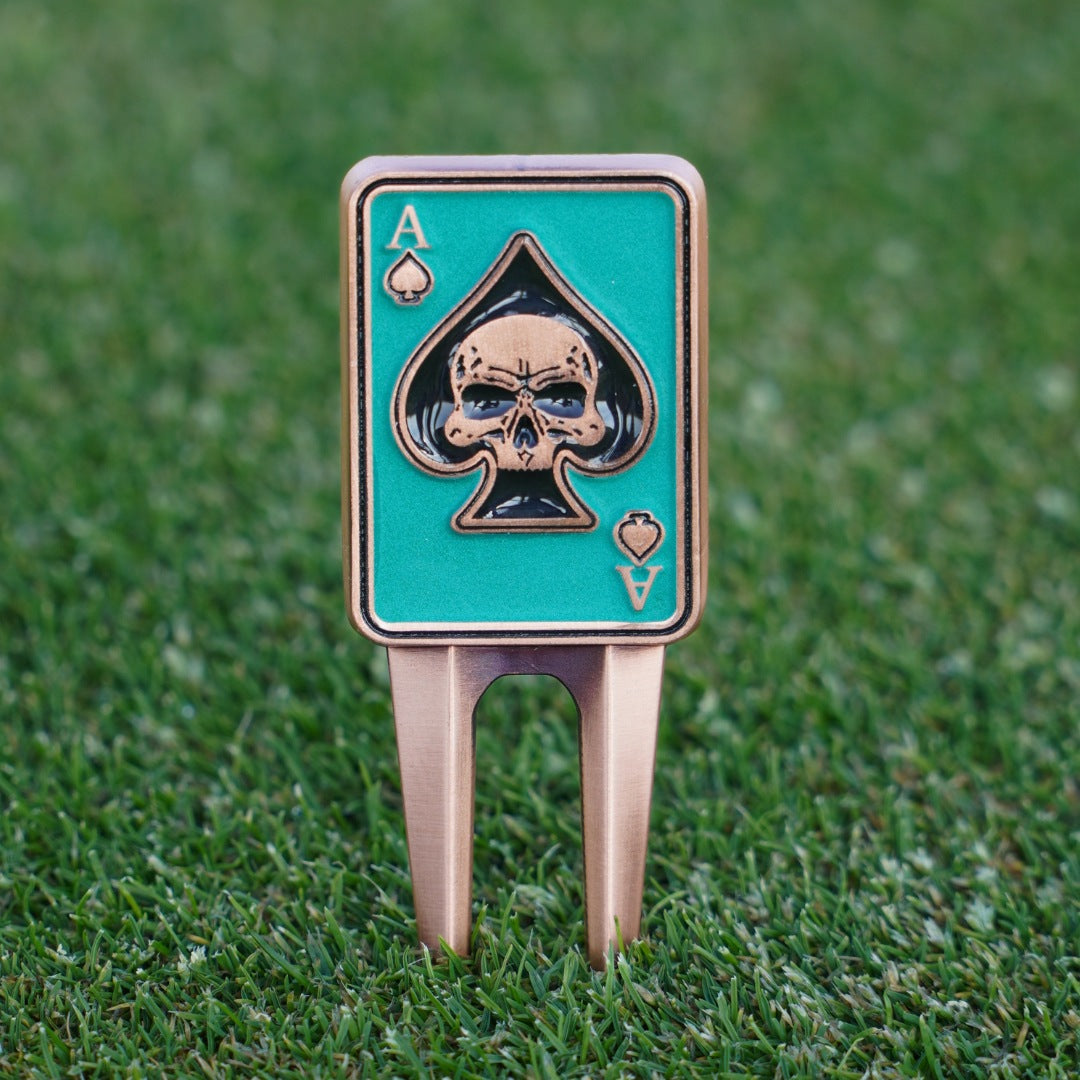 Golf divot tool with skull and ace of spades design on a grass background
