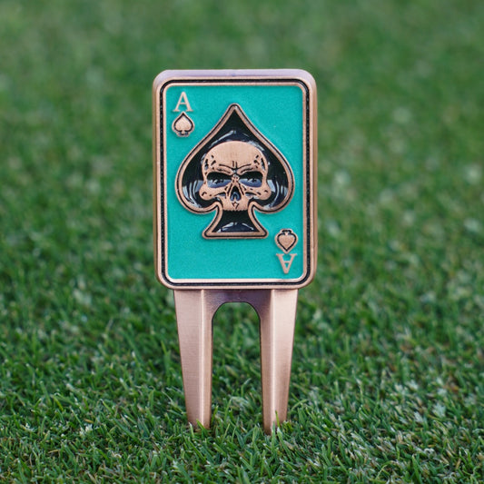 Golf divot tool with skull and ace of spades design on a grass background